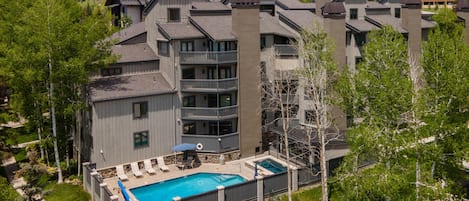 Un hotel de varios pisos con piscina, mobiliario exterior y vistas a las colinas circundantes.