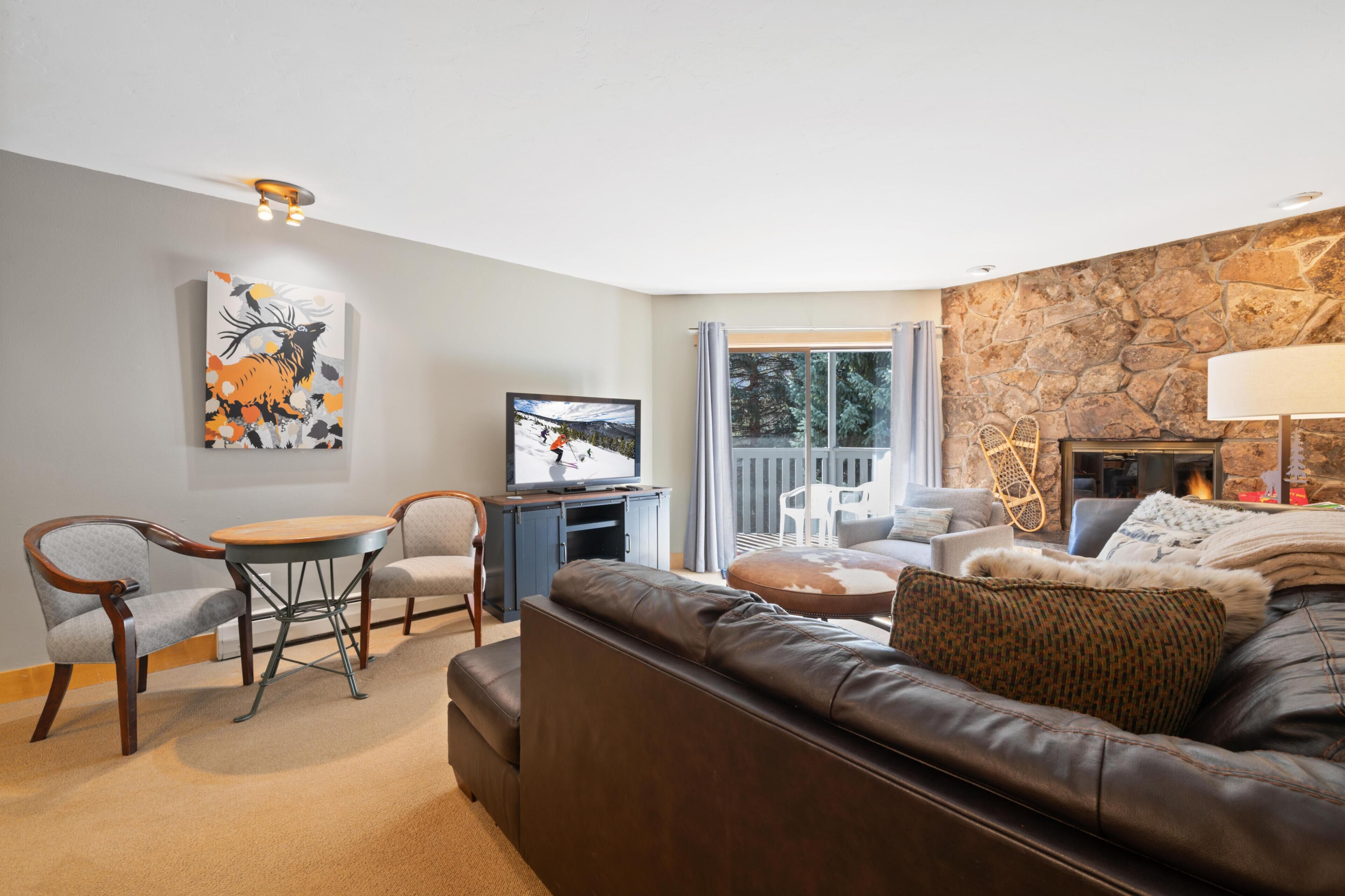 Una sala de estar con pared de piedra, chimenea, televisor y comedor con sillas y mesa.