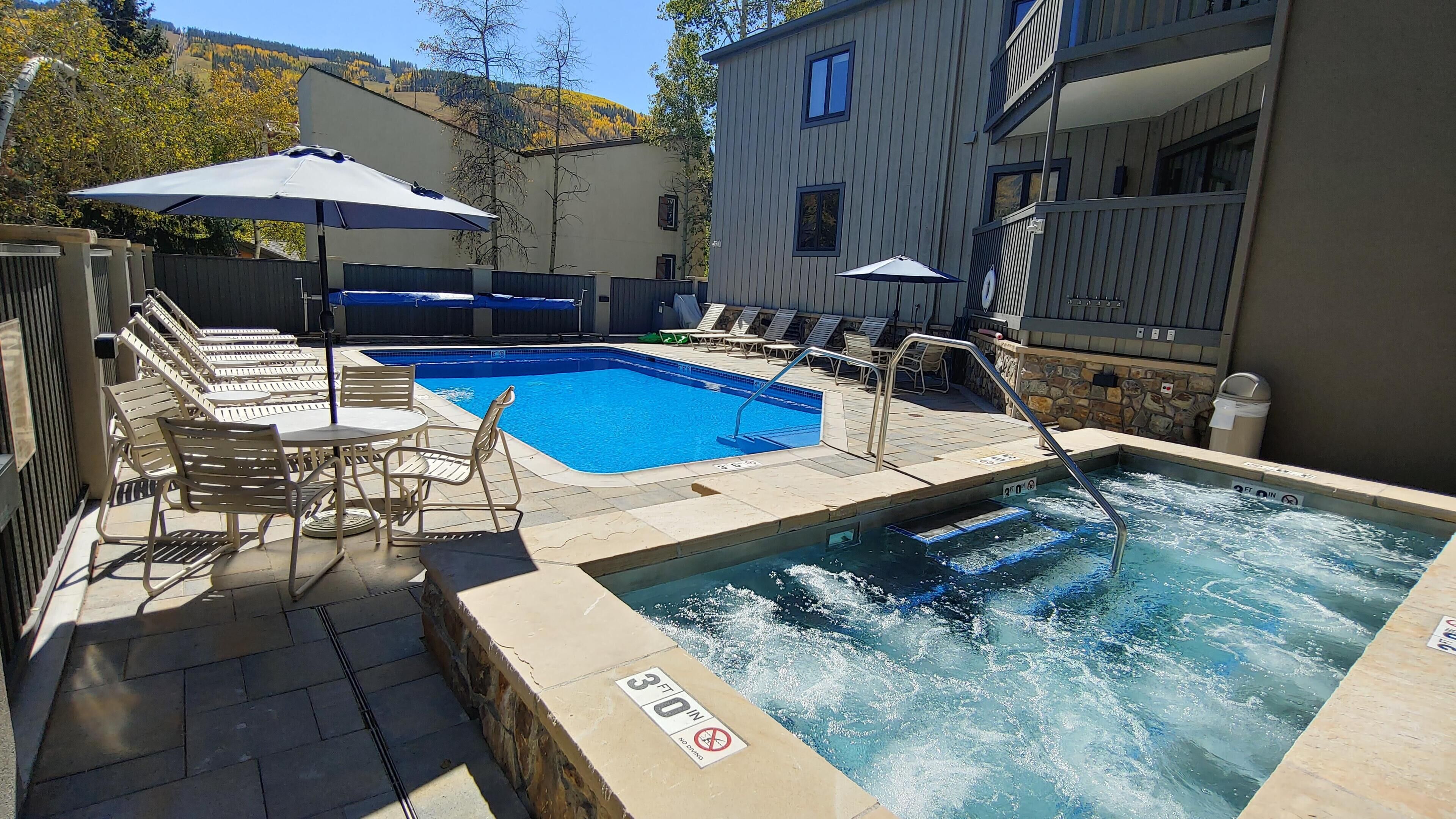 Un área de piscina con sillones de descanso, un jacuzzi y una pared de piedra.