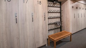 Une rangée de casiers en bois numérotés de 16 à 23, un banc et un porte-manteau fixé au mur.