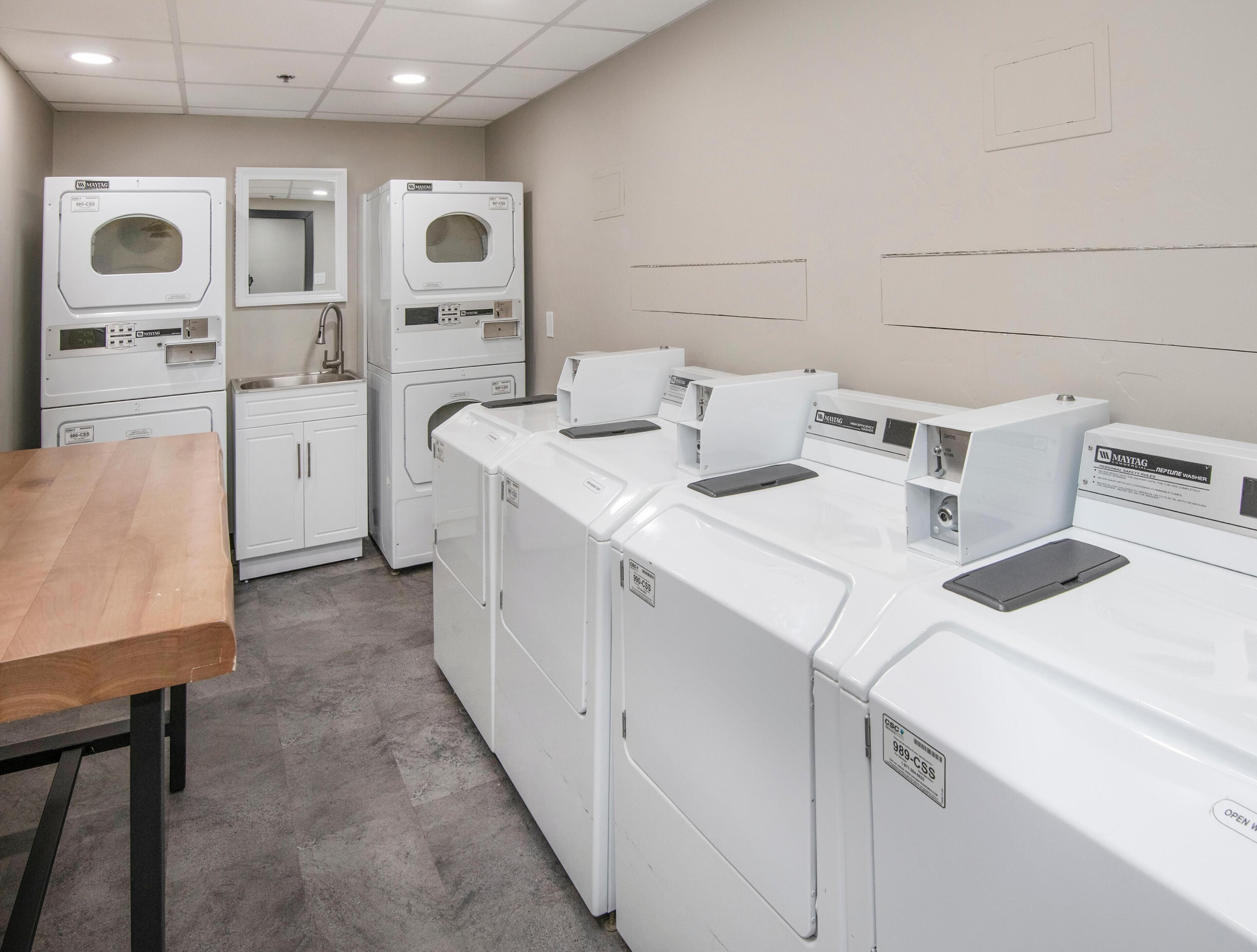 A laundry facility with multiple washing machines and dryers, a sink, and a wooden table.