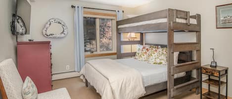 Una litera con ventana, una silla, un aparador y una mesita de noche con lámpara.
