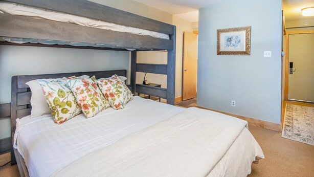 Ein Stockbett mit weißer Matratze, blumigen Kissen und einem Holz-Kopfteil.