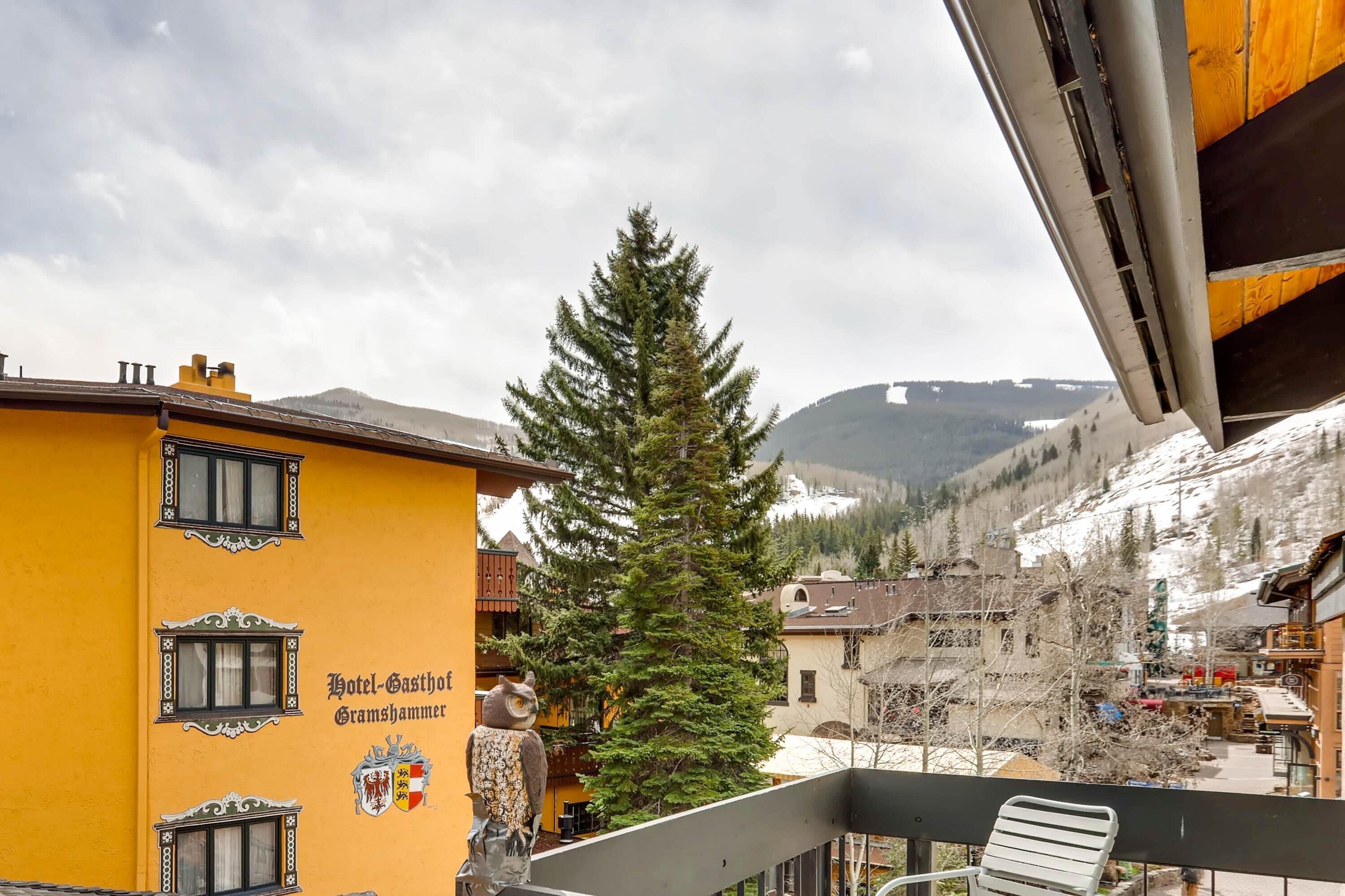 Um edifício amarelo com varanda, brasão e vista para uma montanha nevada.