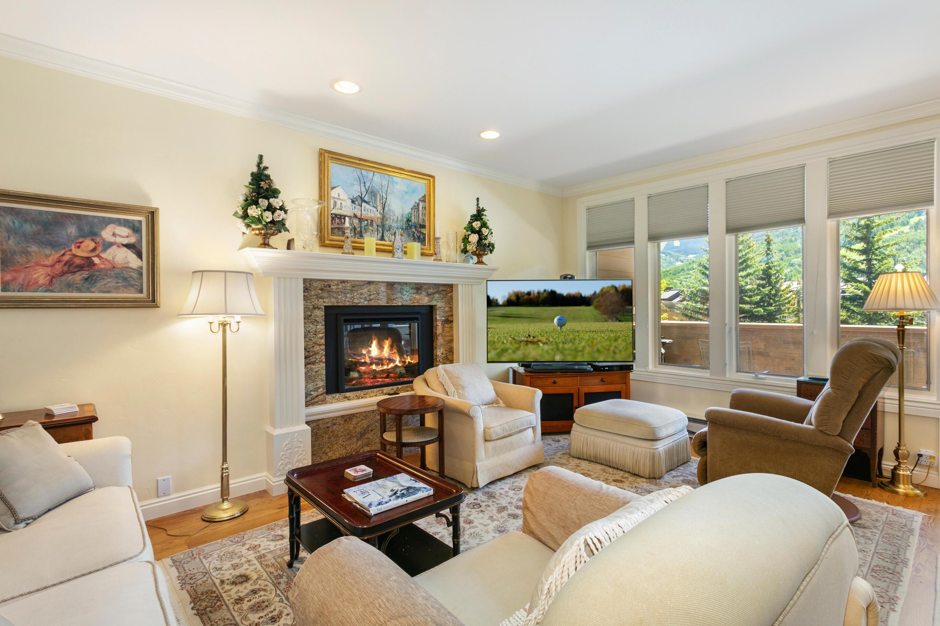 A living room with a fireplace, comfortable seating, a television, and a view of a golf course.
