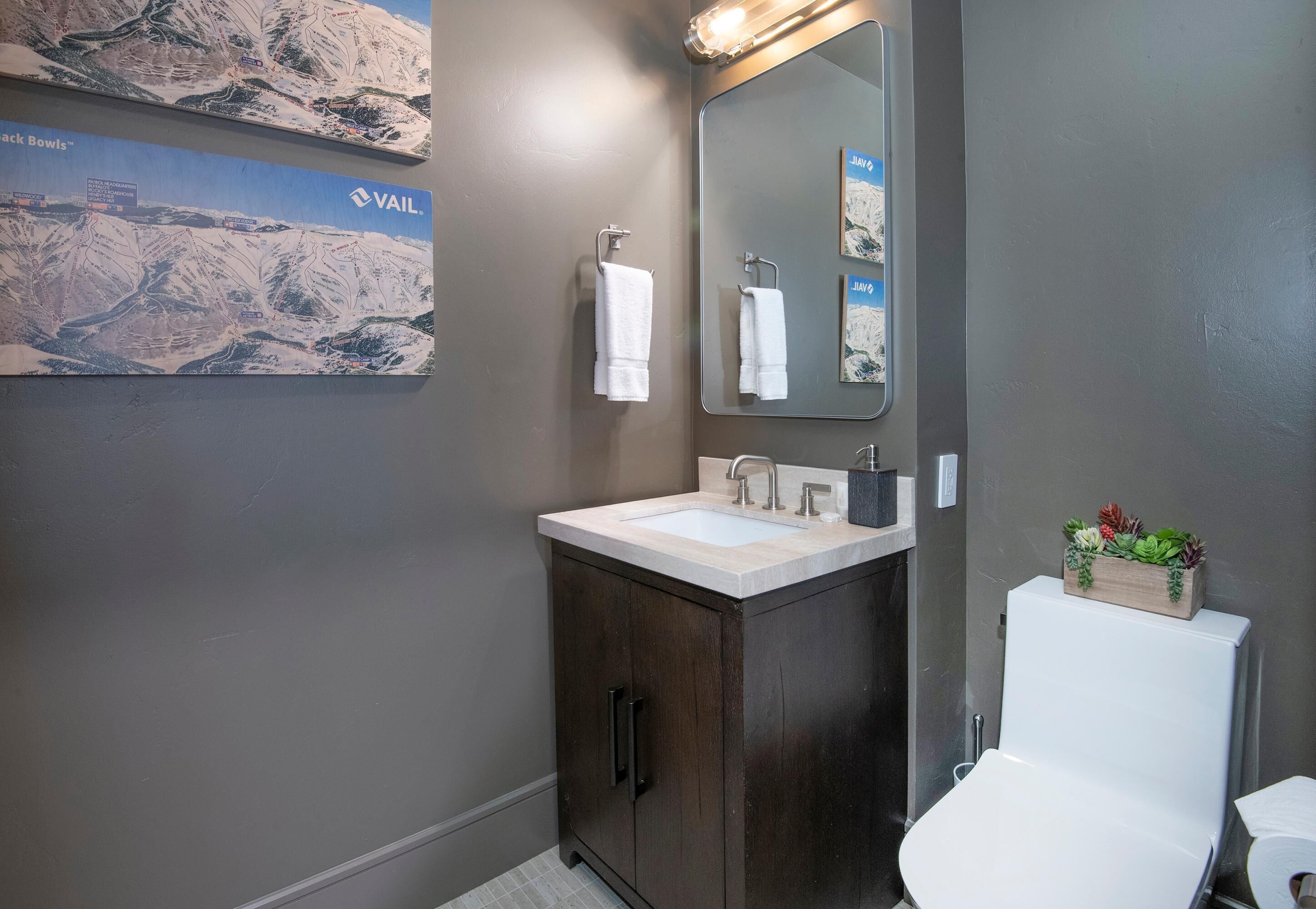 Un baño con un mueble de madera oscura, un lavamanos blanco, un espejo y un inodoro.