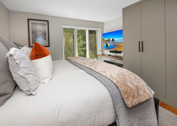 Ein Schlafzimmer mit Bett, Fernseher, Kleiderschrank und einem Fenster mit Blick ins Freie.
