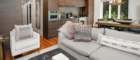 A modern living room with a sofa, armchair, and a dining area with a table and chairs.