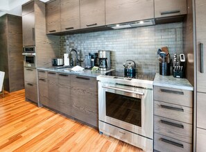 Eine moderne Küche mit Holzschränken, einem Edelstahlbackofen und einer gefliesten Spritzschutzwand.