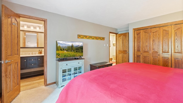 A bedroom with a large bed, wooden wardrobe, a TV, and a bathroom with a mirror and sink. - Westwind 309 1BD 2BA Platinum Condo in Lionshead Village (Vail)