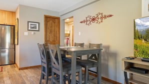 A dining area with a wooden table and chairs, a refrigerator, and a decorative wall piece. - Westwind 309 1BD 2BA Platinum Condo in Lionshead Village (Vail)