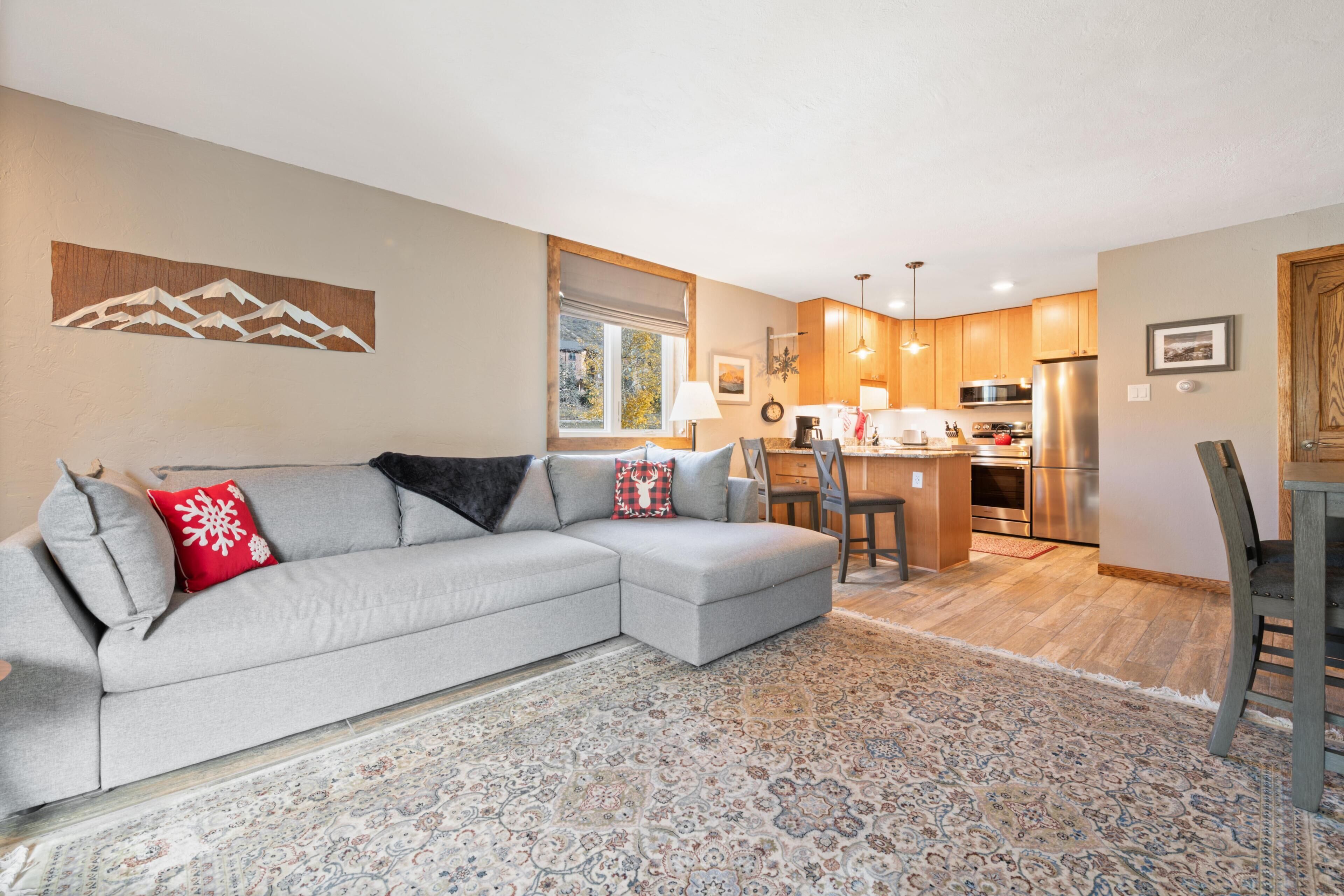 A modern living room with a sectional sofa, a patterned rug, and a kitchen in the background.