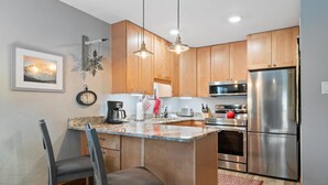 A modern kitchen with wooden cabinets, stainless steel appliances, a granite countertop, and a bar stool. - Westwind 309 1BD 2BA Platinum Condo in Lionshead Village (Vail)