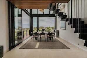 Un espace repas moderne, doté d’une grande table, de chaises et offrant une vue sur l’extérieur.