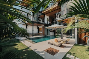 Une maison moderne à plusieurs étages, dotée d’une piscine, d’un espace de détente extérieur et d’une végétation luxuriante.