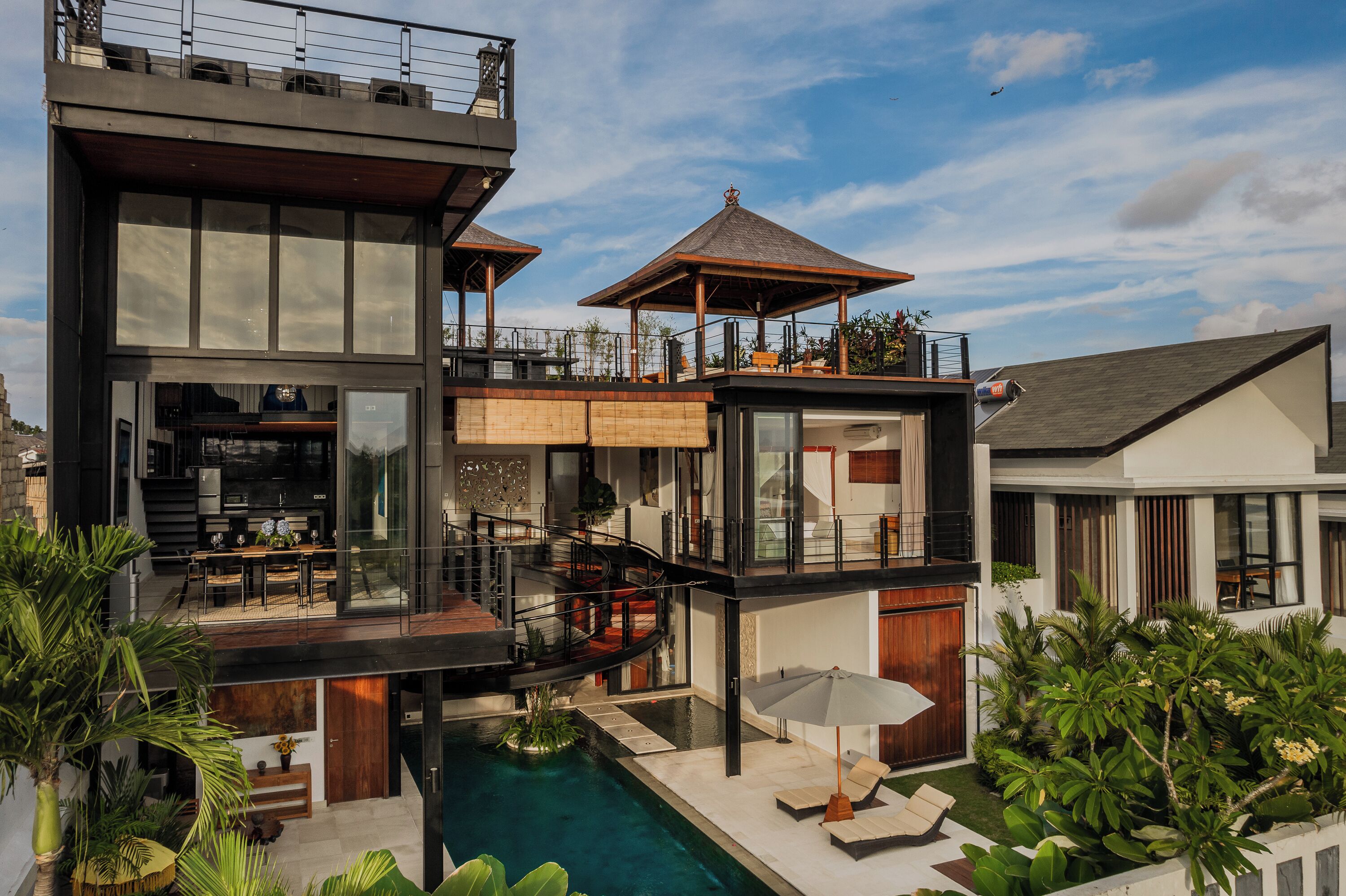 Une maison moderne à plusieurs étages, dotée d’une piscine, d’un espace salon extérieur et d’un patio couvert.