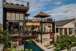 Una casa moderna de varios pisos con piscina, mobiliario exterior y un patio cubierto.