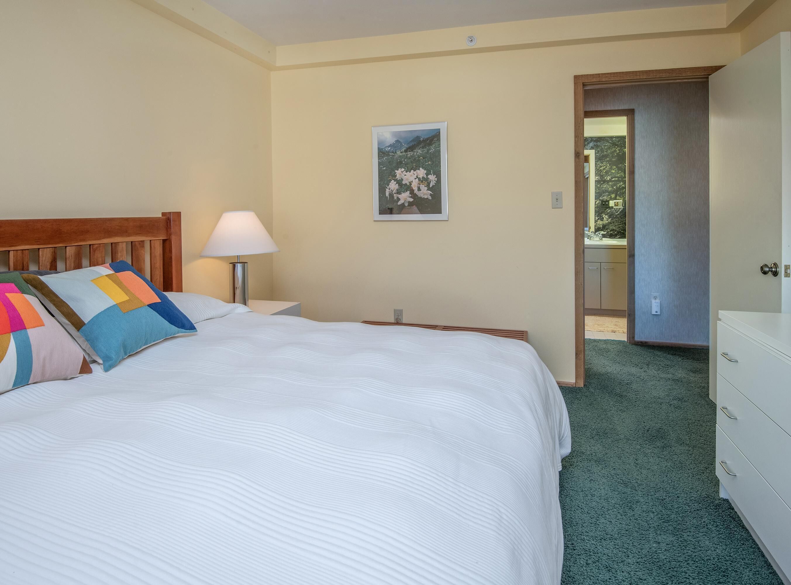 A bedroom with a bed, a nightstand, a lamp, a dresser, and a door leading to a balcony.