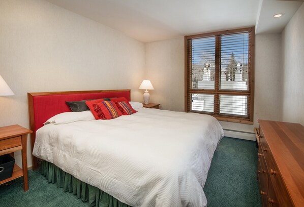 A neatly made bed with a red headboard, a bedside lamp, and a window with blinds. - Treetops 6A, 3BD Ski-in Ski-out Condo (Vail)
