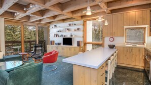 A modern kitchen with wooden cabinets, a central island, and a dining area with a red chair. - Treetops 6A, 3BD Ski-in Ski-out Condo (Vail)