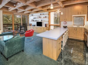 A modern kitchen with wooden cabinets, a central island, and a dining area with a red chair. - Treetops 6A, 3BD Ski-in Ski-out Condo (Vail)