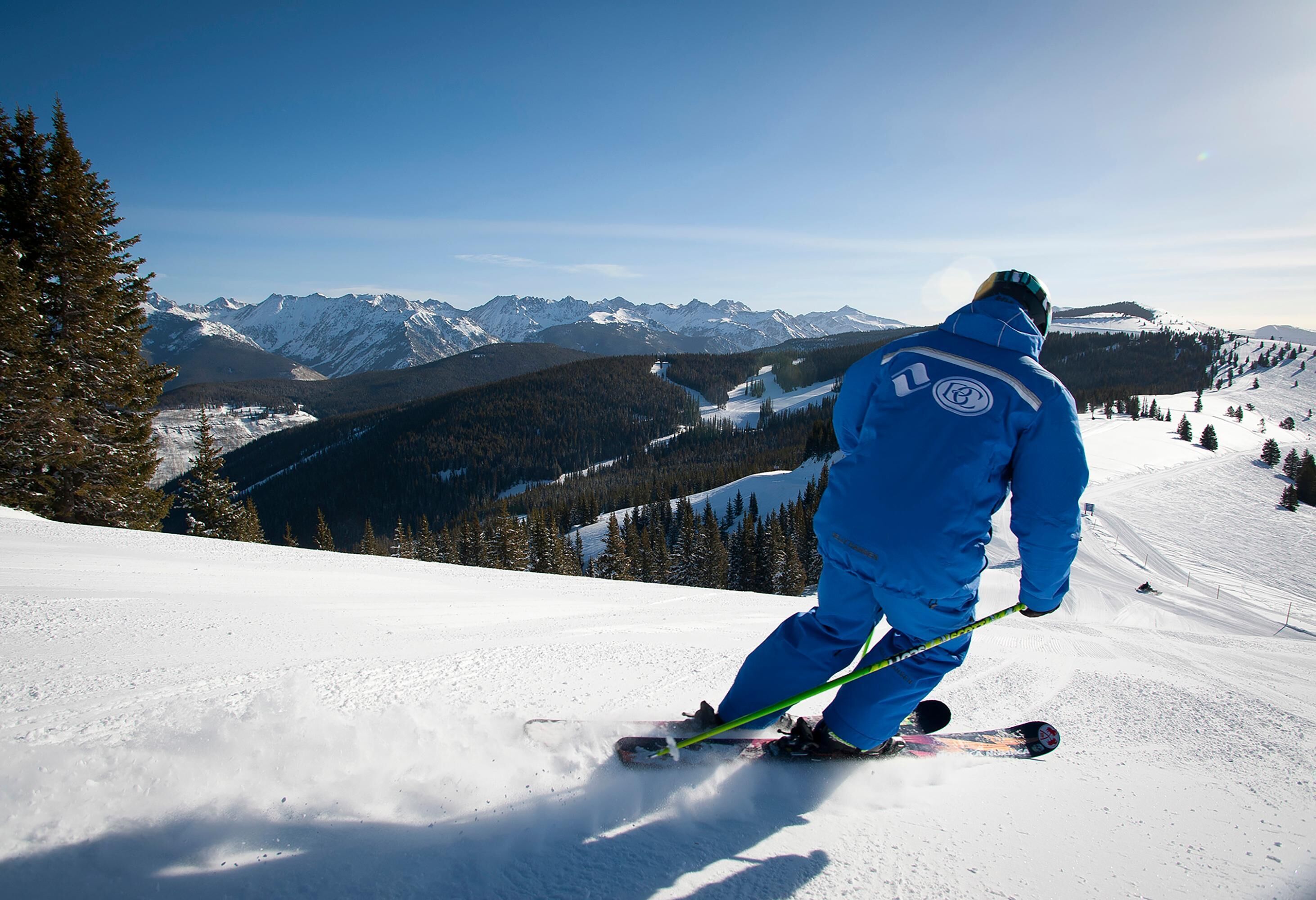 A person skiing on a snowy slope with mountains in the background.