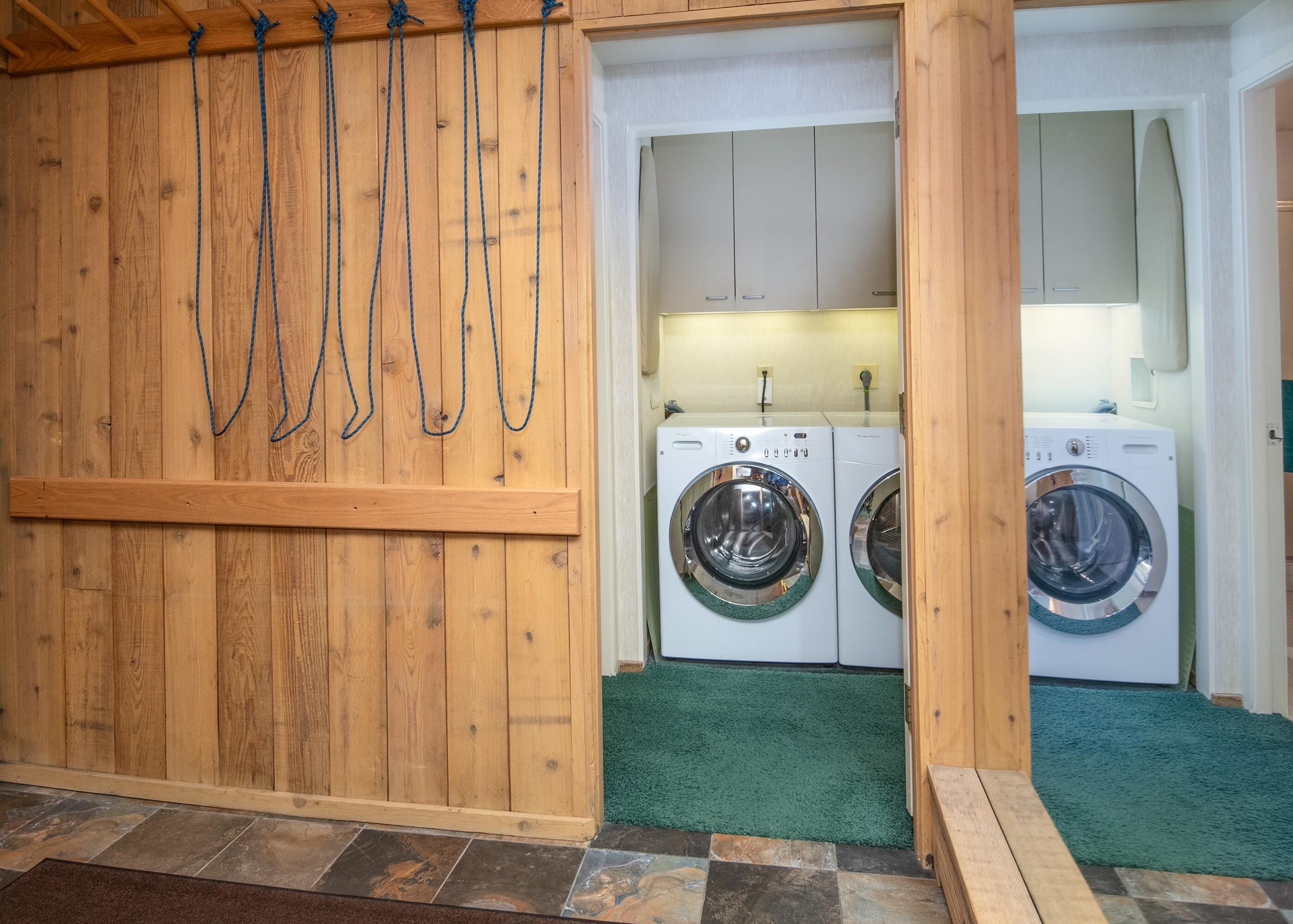Une buanderie avec deux machines à laver, des murs en bois et une moquette verte.