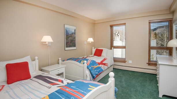 A bedroom with two beds, a desk, a chair, a lamp, and a window with blinds. - Treetops 6A, 3BD Ski-in Ski-out Condo (Vail)