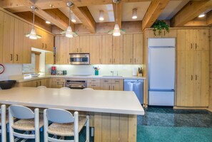 A kitchen with wooden cabinets, a white island, stainless steel appliances, and hanging pendant lights. - Treetops 6A, 3BD Ski-in Ski-out Condo (Vail)