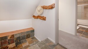 Un pasillo con un banco, un sombrero colgado en la pared y un objeto de madera.
