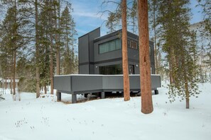 A modern, multi-story building with a flat roof, surrounded by tall pine trees in a snowy landscape. - Gore Circle Chalet, 4BD Private East Vail Home (Vail)