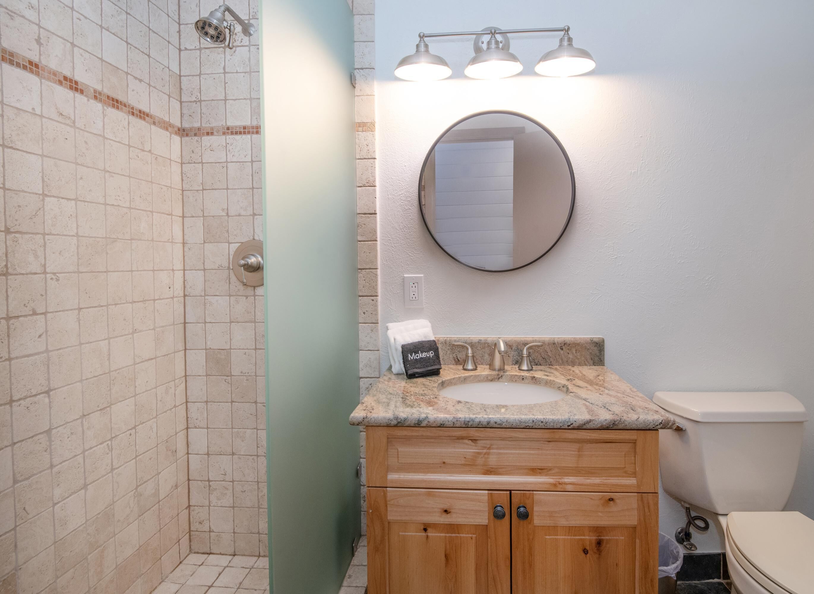 Ein Badezimmer mit Dusche, Waschbecken, Spiegel mit Beleuchtung und Toilette.