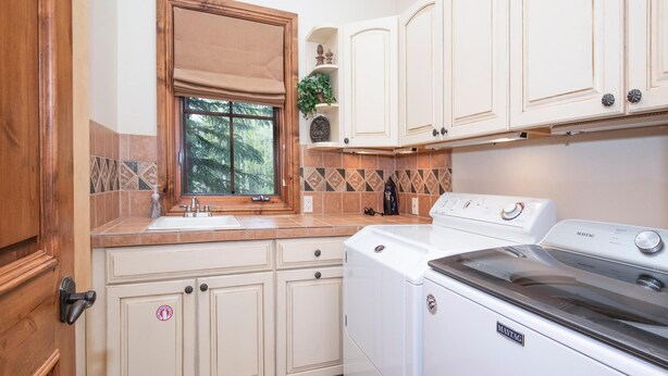 A kitchen with a built-in washer and dryer, a window with a beige blind, and a tiled backsplash. - 796a Potato Patch - 4BD Private Home in Vail (Vail)
