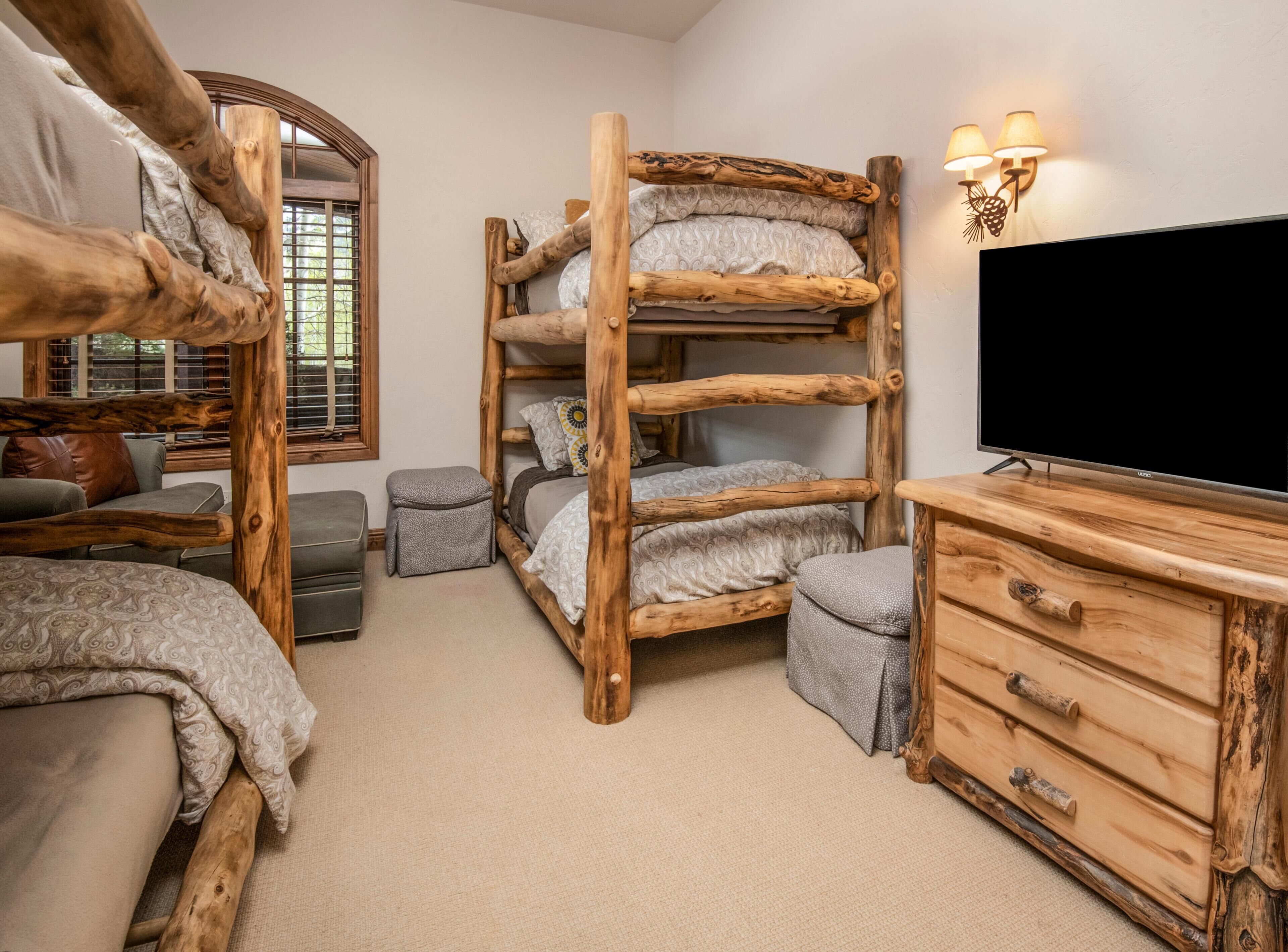 A bunk bed room with a TV, wooden furniture, and a window with blinds.