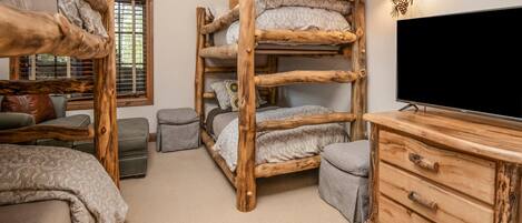 A bunk bed room with a TV, wooden furniture, and a window with blinds.