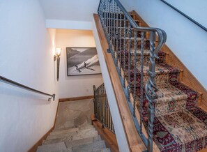 Eine Treppe mit gemustertem Teppich, einem hölzernen Geländer und einer Wandleuchte.