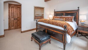 A bedroom with a large bed, a wooden bench, a nightstand, a lamp, a painting, and a wooden door. - 796a Potato Patch - 4BD Private Home in Vail (Vail)