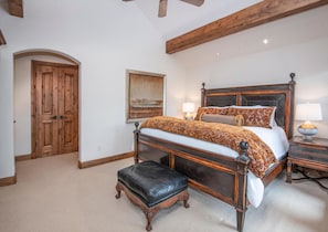 Ein Schlafzimmer mit einem großen Bett, einer hölzernen Bank, einem Nachttisch, einer Lampe, einem Gemälde und einer Holztür.