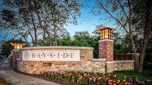 A stone wall with a sign reading "BAYSIDE" and a brick building with a lighted tower. - Bayside Resort Escape: 5BR Coastal Home -Golf, Pools, Restaurants & Beach Access (Selbyville)