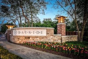 A stone wall with a sign reading "BAYSIDE" and a brick building with a lighted tower.