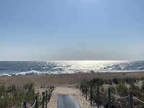 A beach pathway leading to the ocean with a clear sky.