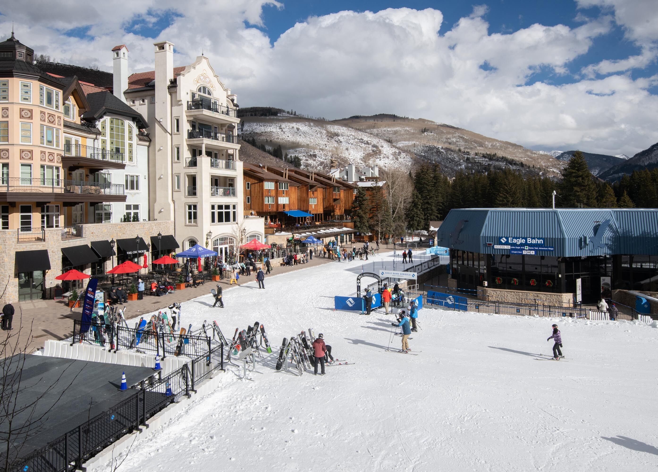 Ein Skigebiet mit einer Seilbahn, einem Gebäude mit der Aufschrift 'Eagle Bahn' und einem schneebedeckten Berg im Hintergrund.