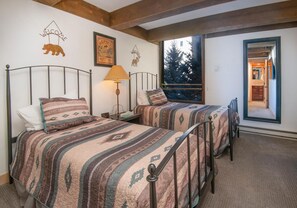 Ein Zimmer mit zwei Betten mit Metallgestell, einem Fenster mit Blick auf Bäume und einem 'WELCOME'-Schild an der Wand.