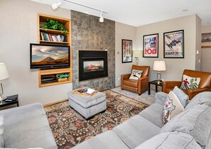 A living room with a fireplace, a television, a bookshelf, and a couch. - Sun Vail 13e, 2bd, 2BA Condo With Vail Mountain Views (Vail)