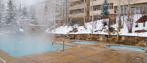 A heated outdoor pool area with stone walls and a view of a multi-story building.