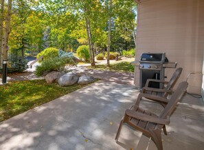 An outdoor patio with a grill, wooden chairs, and a stone pathway leading to a building. - Sun Vail 13e, 2bd, 2BA Condo With Vail Mountain Views (Vail)