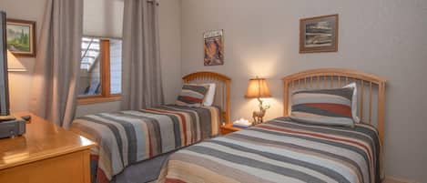 A bedroom with two beds, a desk, a lamp, and a window with curtains.