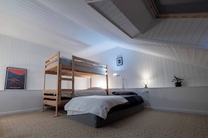 Ein Schlafraum mit Etagenbetten, einer geneigten Decke, einem gerahmten Bild an der Wand, einem Schreibtisch mit Lampe und einem Blumentopf.
