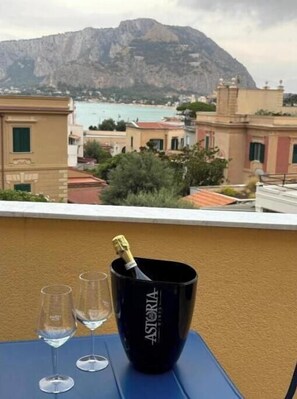 Ein Tisch mit einer Astoria-Weinflasche, zwei Gläsern und Blick auf eine Küstenstadt mit Häusern und einem Berg.