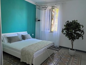 Ein Schlafzimmer mit Bett, einem Fenster mit Vorhängen, einem Heizkörper und einer Zimmerpflanze.